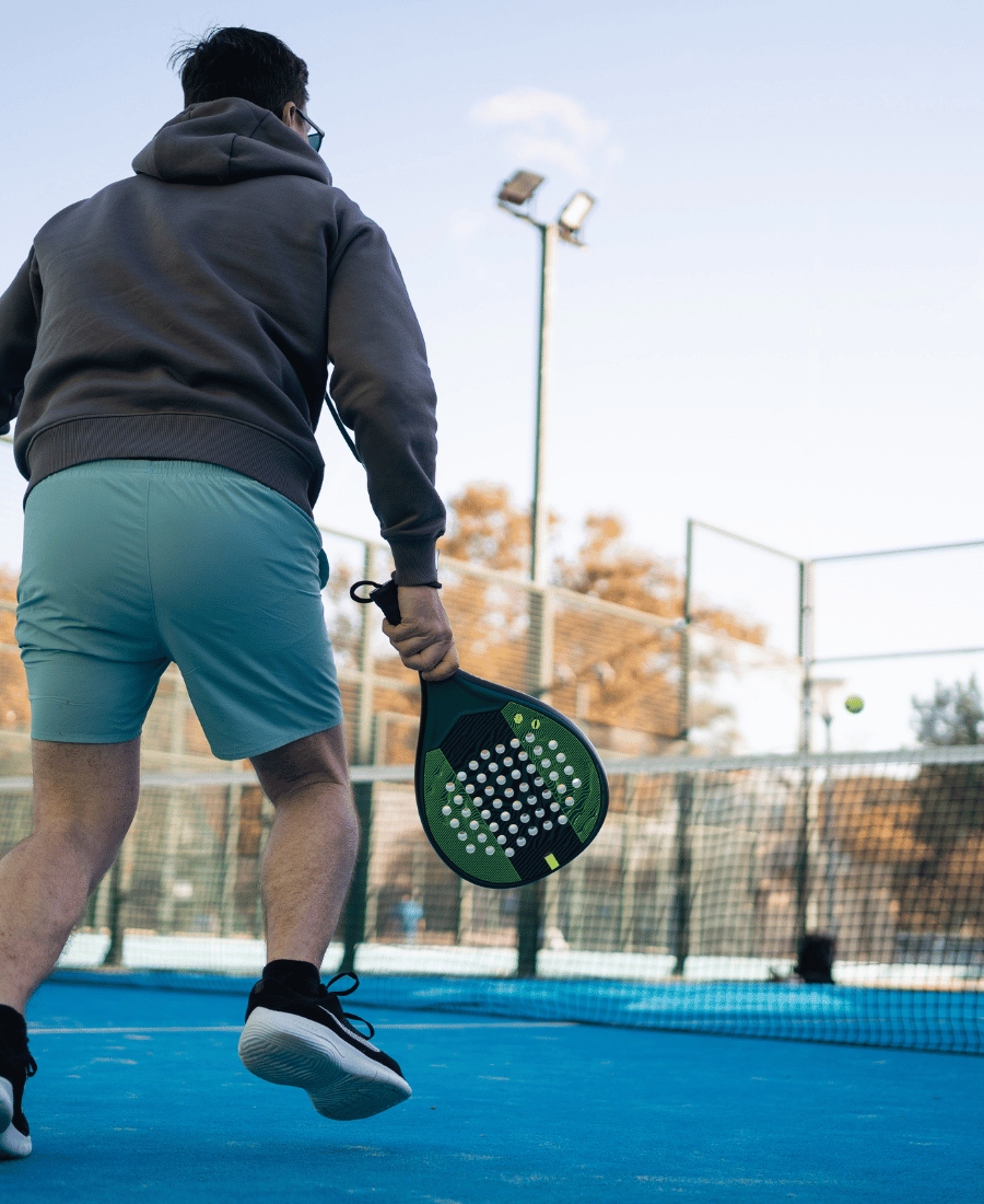 A Man Prepares for a Backhand Shot in Padel Tennis, with a Focused Expression and the Court's Fence Shadow Patterned on the Ground