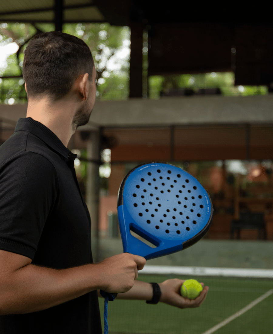 Man Holding a Blue Padel Racket and Yellow Ball on Court